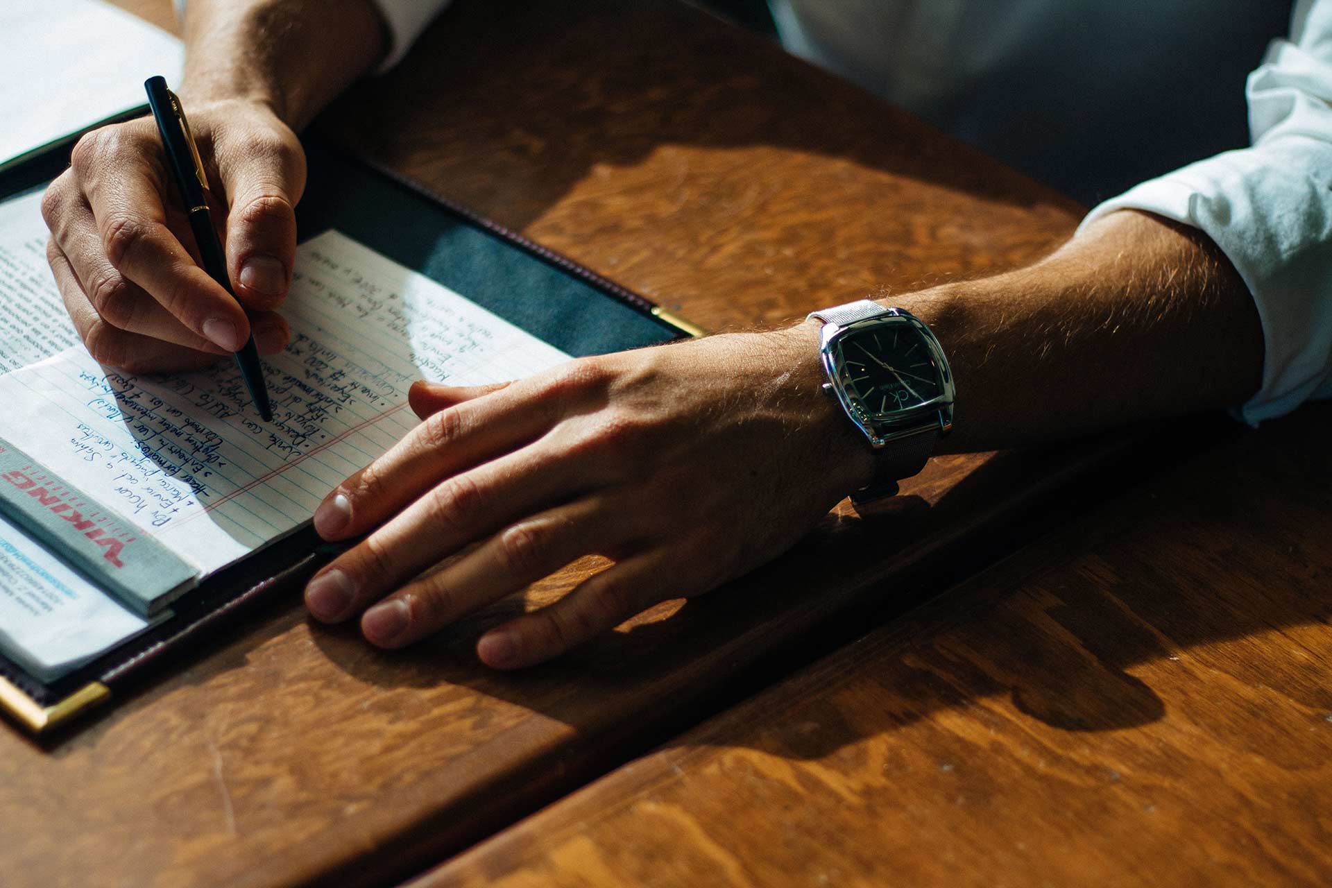 Two male hands on table, writing on paper